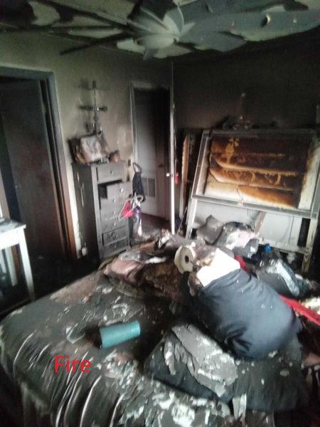 Fire-damaged bedroom showing charred furniture collapsed ceiling and extensive soot damage